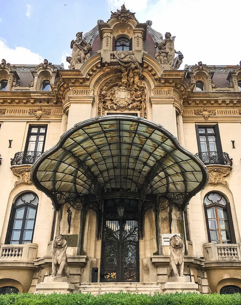 An elaborate pink building with tall windows, a shell shaped glass portico, decorative door and guardian stone lions