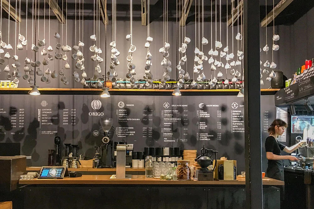 An interior shot of a barista making coffee inside a dark modern, cafe decorated with hanging coffee cups