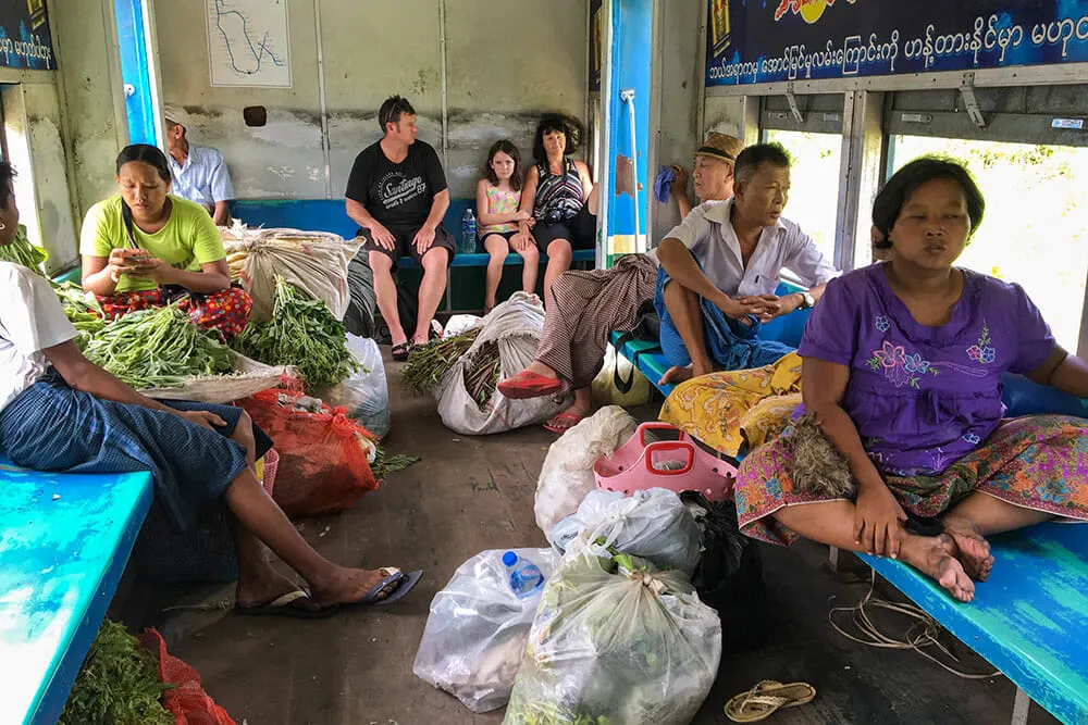 locals and tourists sitting and talking with their baskets of fruits and vegetables in train on circle line in Yangon