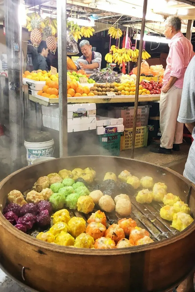Dumplins in bamboo steamer with a fruit market stall in the background