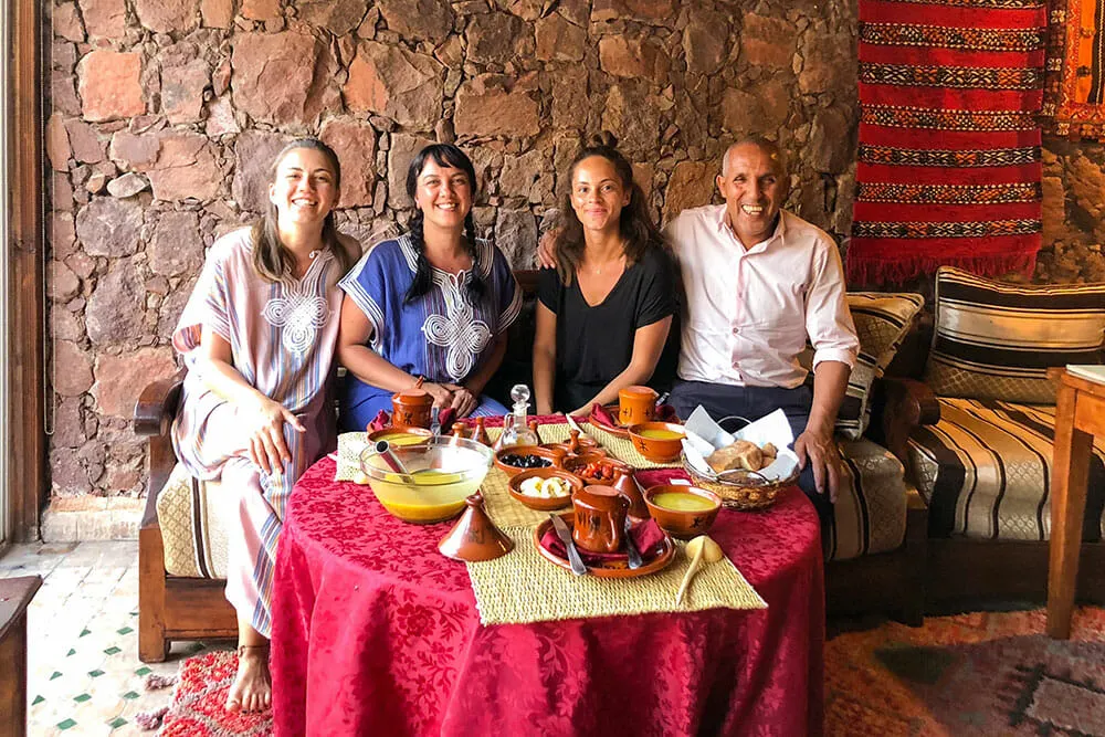 Three female friends sitting with a male host ready for dinner with food on the table