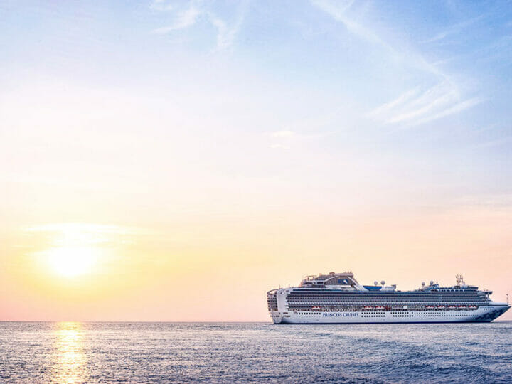 A beautiful pink, sun-flooded image of a white multi-decked cruise ship out to sea