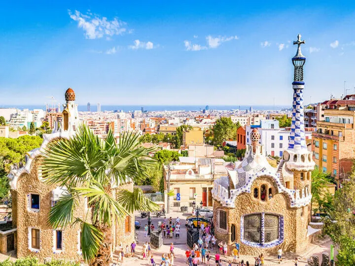 A view across the top of the city to the sea, a park in the fore where sculpured, mosaic-tiled buildings stand with pretty blue and white domes and minarets