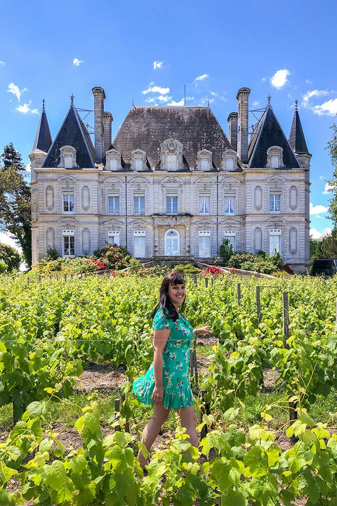 Me in the middle of rows of young grapevines in front of a beautiful chateau with tall chimneys