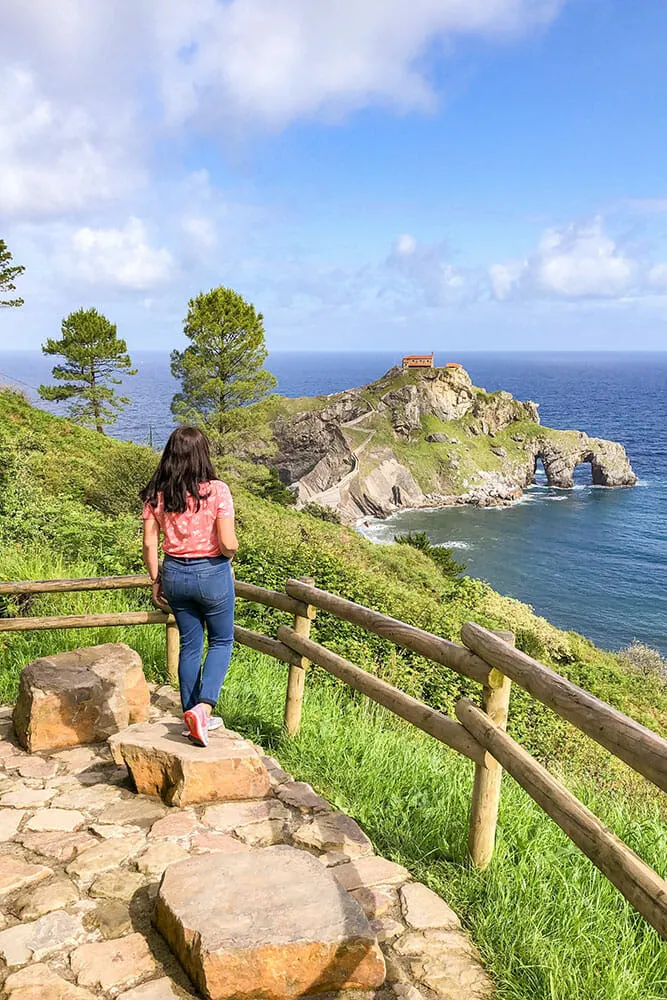 Me standing on a pink rock path on a grassy cliff looking out to sea at a tied island