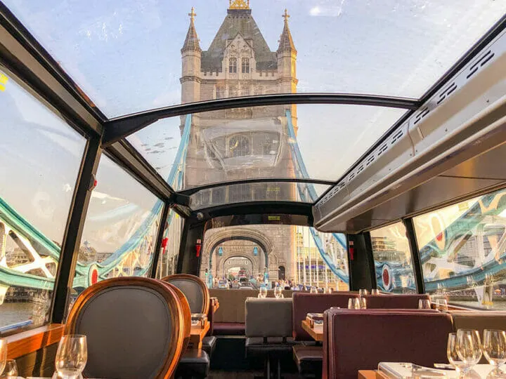 View of Tower Bridge from inside a glass roofed bus as it drives through the bridge. The Bus has tables set for dinner and it's a unique way to see London