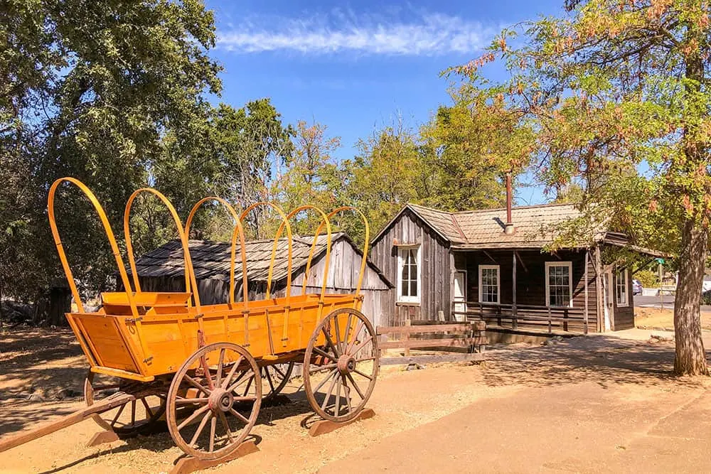 Old fashioned wagon cart and a small wooden house in Columbia. Visiting Columbia is one of the best things to do in Gold Country, California
