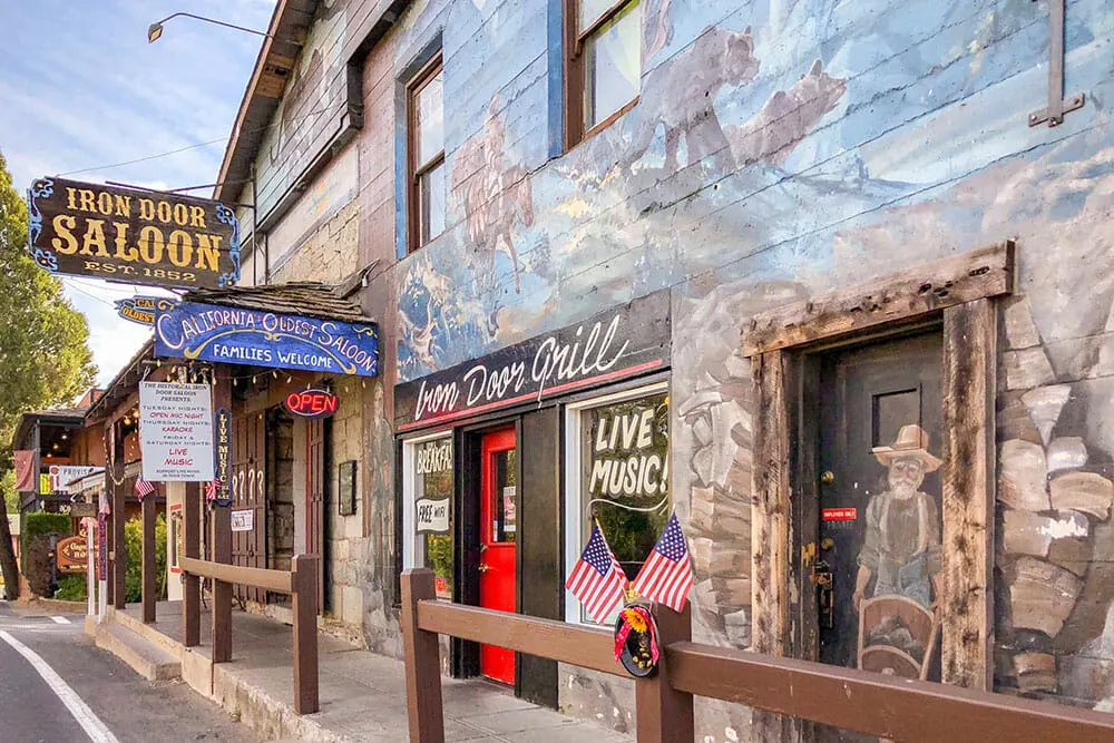 Facade of a building painted with gold mining images with a sign reading Iron door saloon set 1852. Having a drink here is one of the best things to do in Gold Country, California