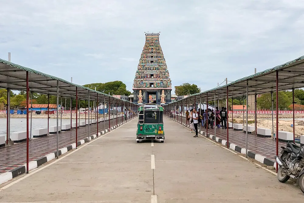 Tuk tuk driving down a straight road towards a hindu temple