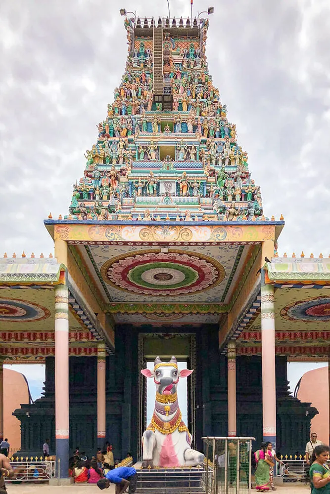 Hindu gate tower decorated in blue and green and a statue of a cow in front of it