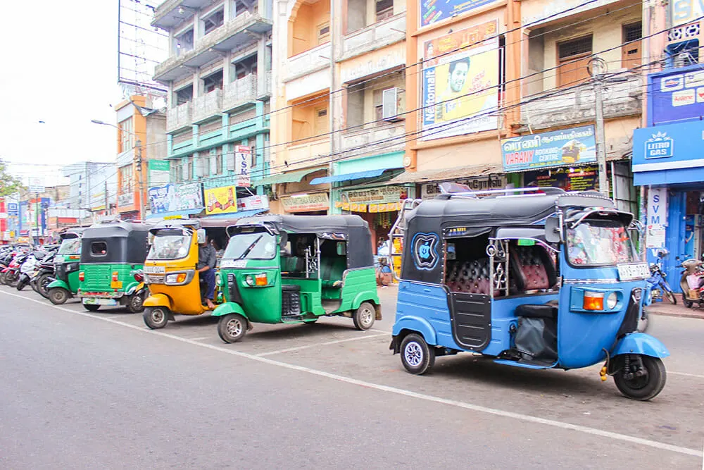 Line of colourful tuk tuks parked on the road with tall buildings behind them