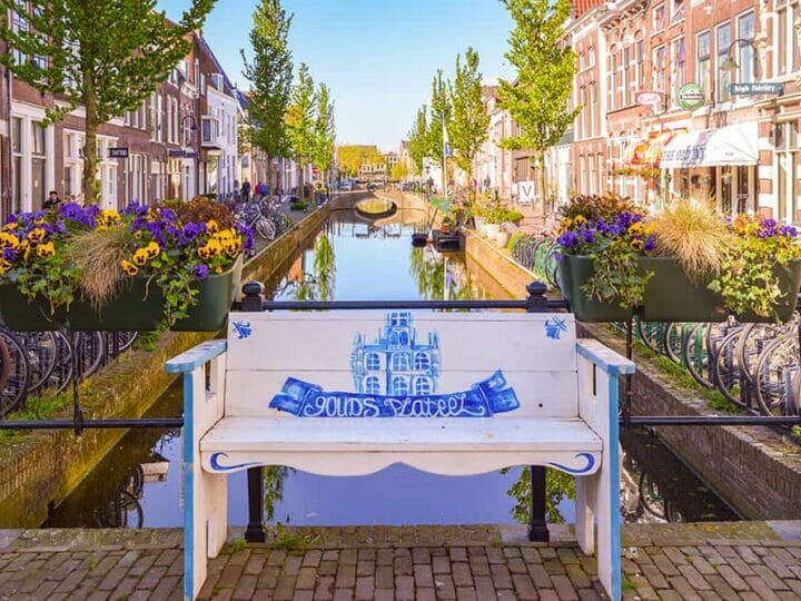 Wooden bench painted white and blue with a canal and typical Dutch houses behind