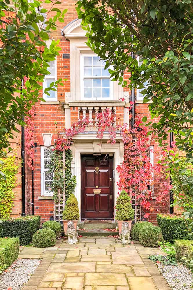 Jolie maison avec la porte d'entrée encadrée de lierre rouge et de buissons topiaires