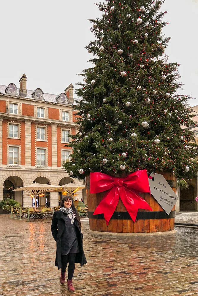 Me walking past a giant Christmas tree with a red bow in a square
