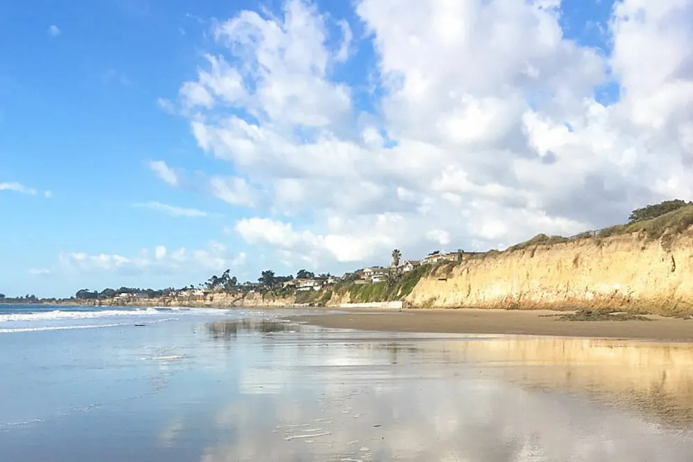 View of a large beach from the shore with the sea on the left and sandstone bluffs on the right