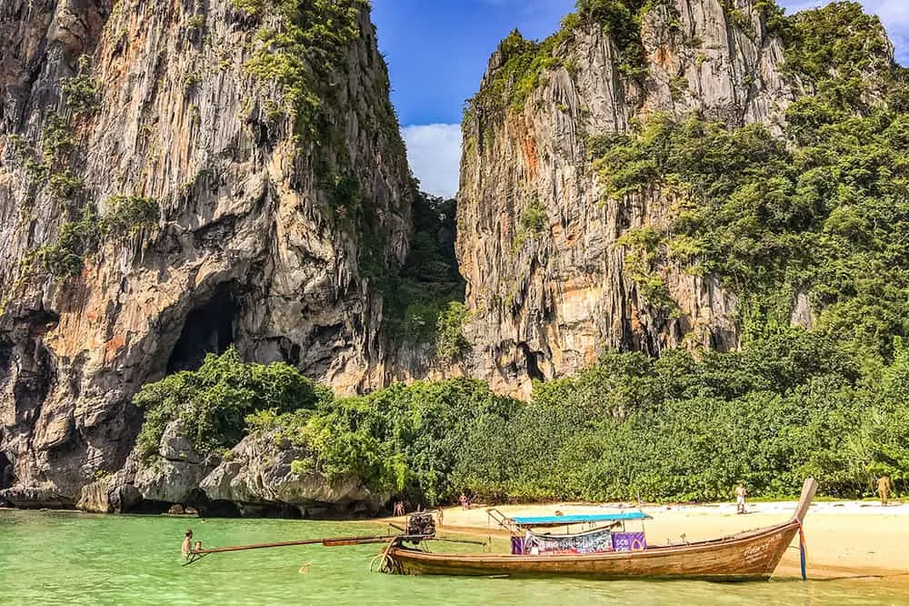 Long tail boat on the shore of a beach with crystal clear water and limestone cliffs in the background