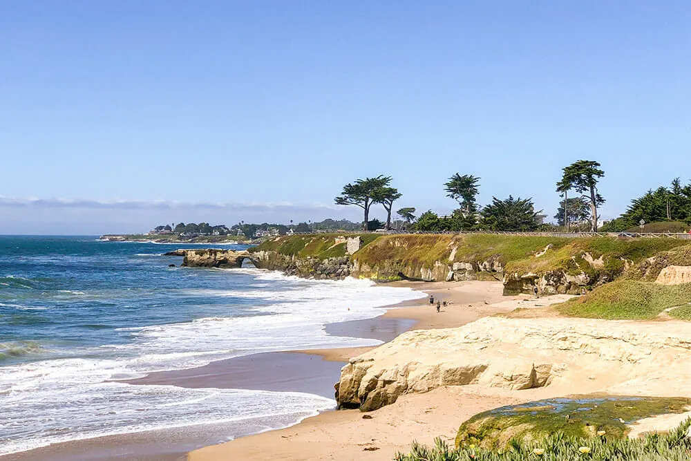 View of a wriggly coastline that follows a golden sand beach. There are trees on a headland in the distance