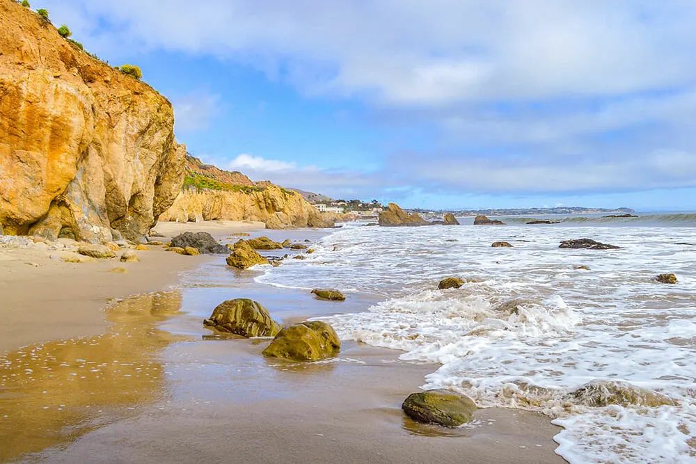 Beach with sandstone bluffs on the left and the ocean on the right. There are small rocks scattered along the shoreline