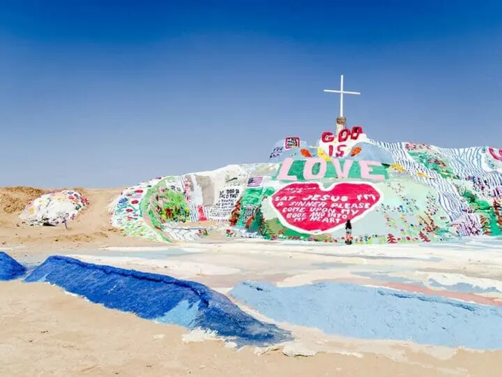 Colourful mount painted with bright colours and messages about God is Love and Jesus. There is a white cross on top of the mount. This is one of the most unique places to visit in california