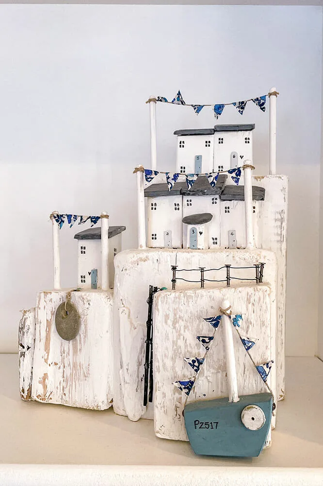 Decorative item made of wood carved in the shape of white fishermen cottages with a blue fishing boat and blue bunting