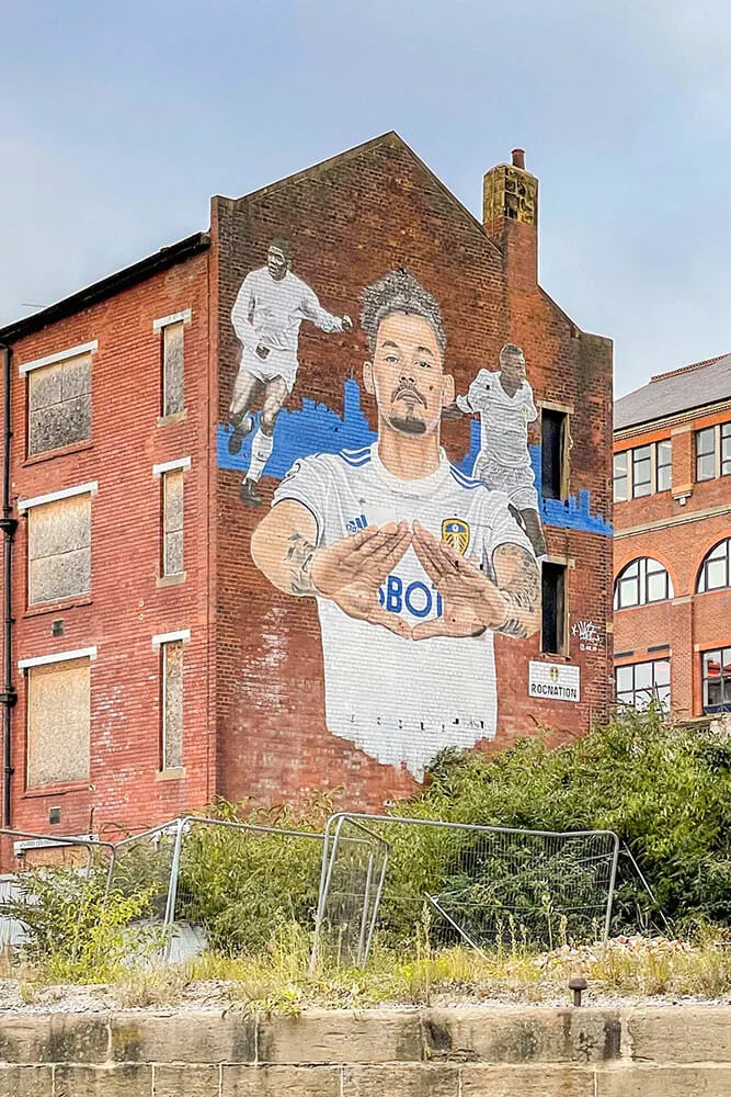 Street art mural of a Leeds footballer on the side of a three storey red brick building that looks abandoned