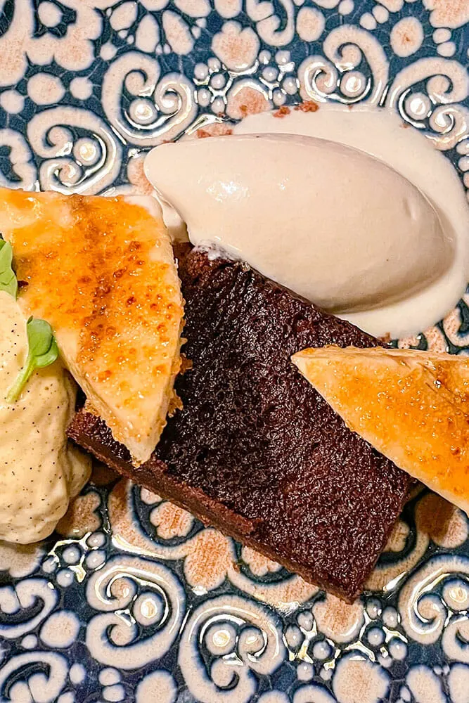 A square of brownie with caramelise banana and ice cream on a blue and white decorated plate