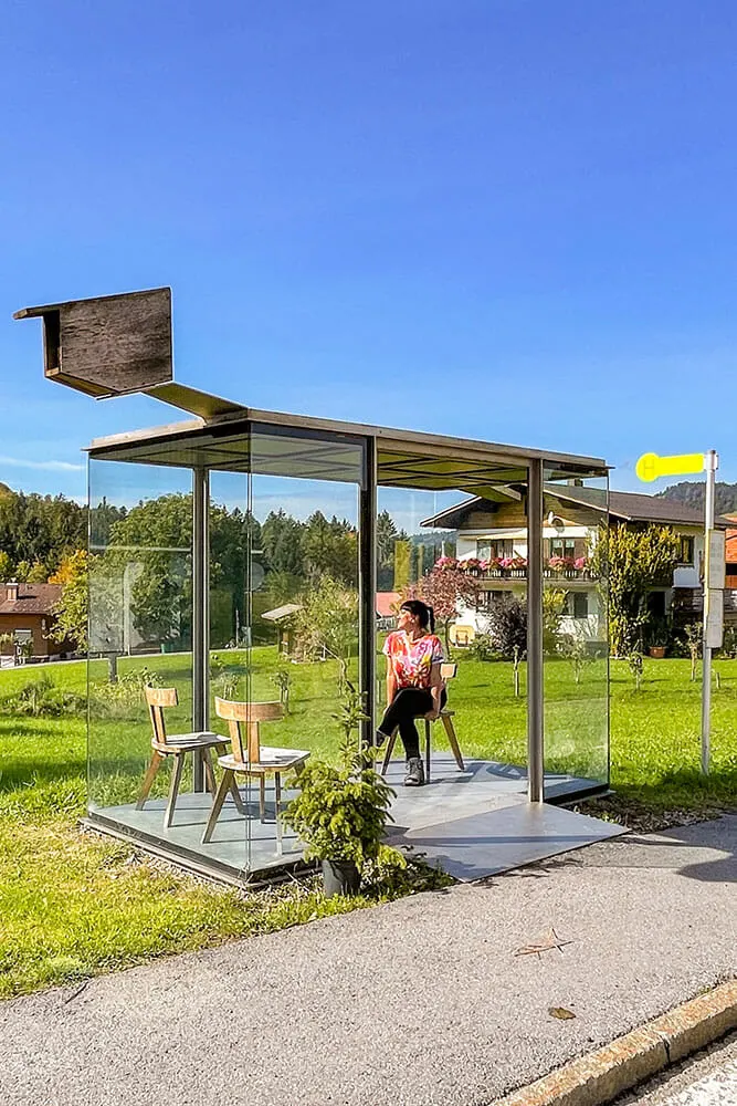 Me sitting on a wooden chair inside a glass box with a bird box on top