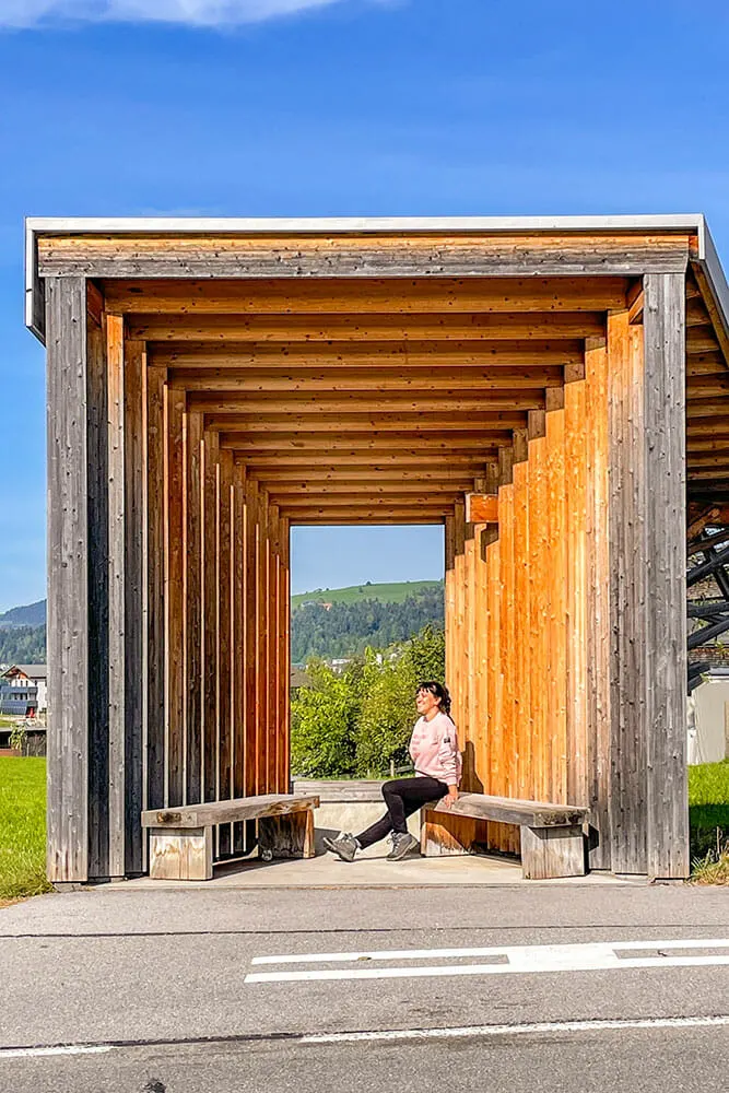 Me sitting on a wooden bench at a bus stop made to look like a camera obscura