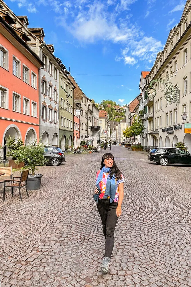 Me standing on a cobblestoned street lined up with Medieval buildings and arcades. There are two ares parked in the street