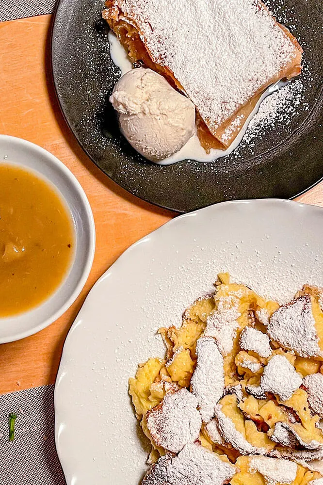 Plates with a strudel with ice cream, apple sauce and kaiserschmarn or broken pancakes dessert. All sprinkled with icing sugar.