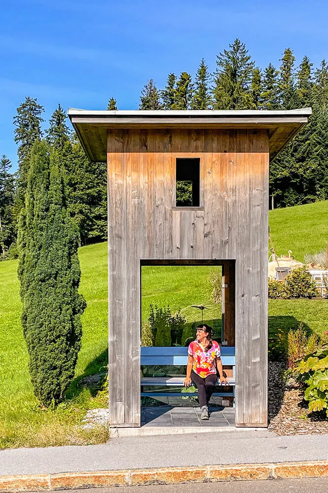 Wooden bus stop made to look like a watchtower. I'm sitting in a blue bench inside the bottom section.