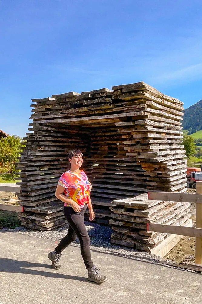 Me walking past a bus stop that has been made of stacked up wooden planks in a Jengga style