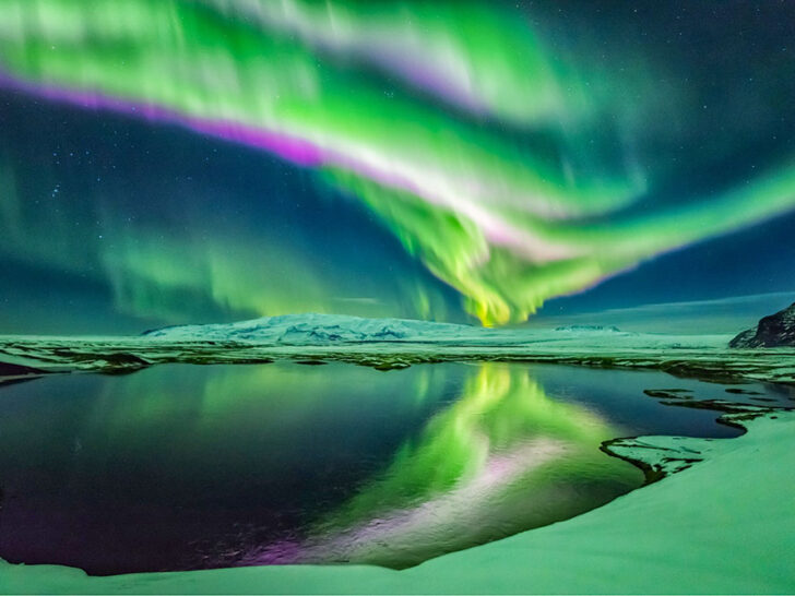 Illuminating lines in the starry skies glowing in green and hints of violet being reflected at the lake below surrounded by snow covered mountains and filled. Watching this is one of the best things to do in Iceland.