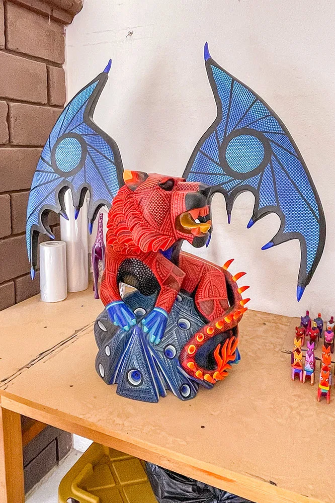 A small sculpture of a red lion with intricate prints and details and blue wings sitting on a wooden table