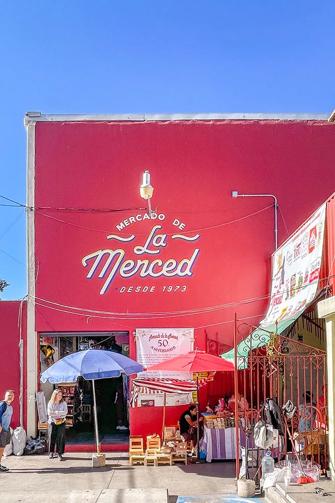 Mercado de La Merced's pink-painted facade with street vendors and people entering and exiting the market.