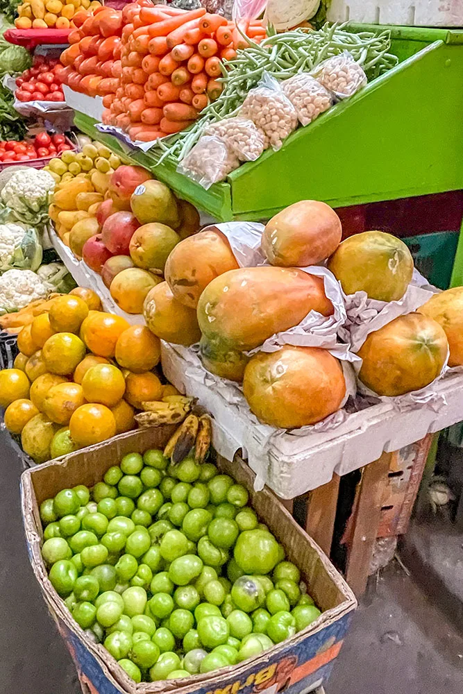vegetables and fruits on display in wooden carts, boxes, and green racks in a local market in Oaxaca