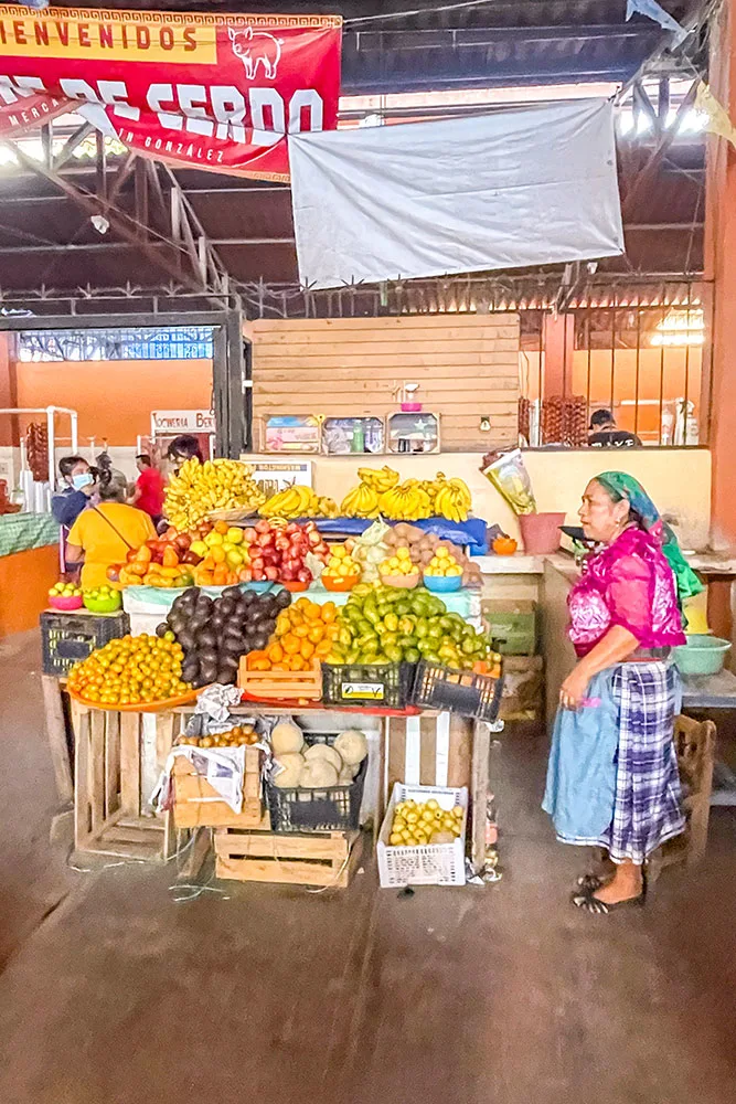 Displays of mangoes, bananas, and other fruits on different wooden crates with people walking in the Tlacolula market