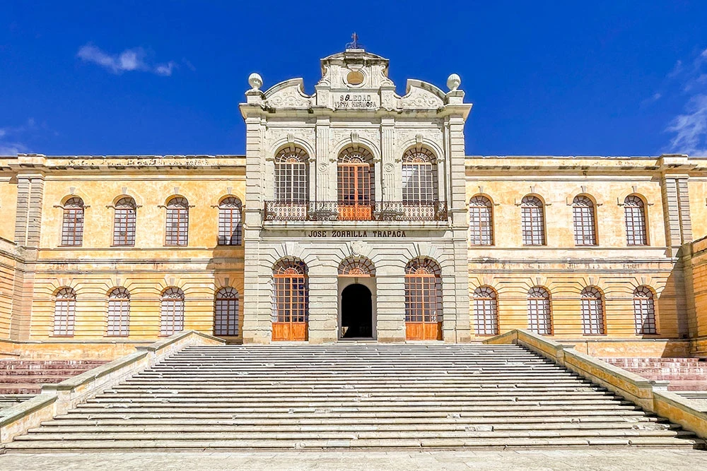 A staircase leading to a long, rectangular building with columns and arches, and a large wooden door at the center of the Centro de las Artes de San Agust&iacute;n. 