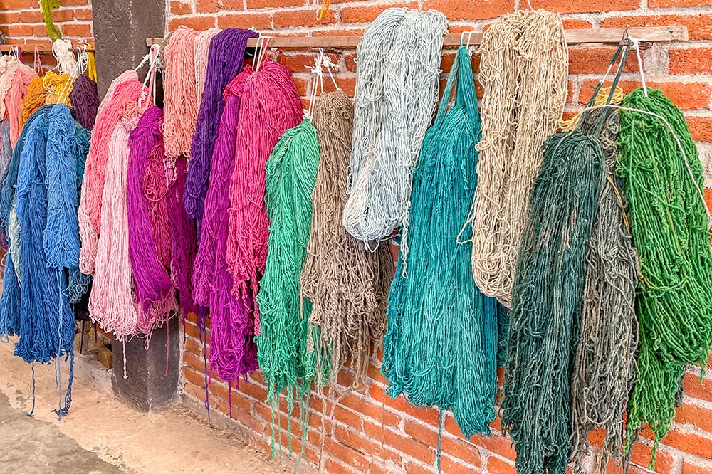 Dyed wool of colors of blue, violet, pink, and yellow hanged on the red bricked wall to see in Oaxaca Mexico