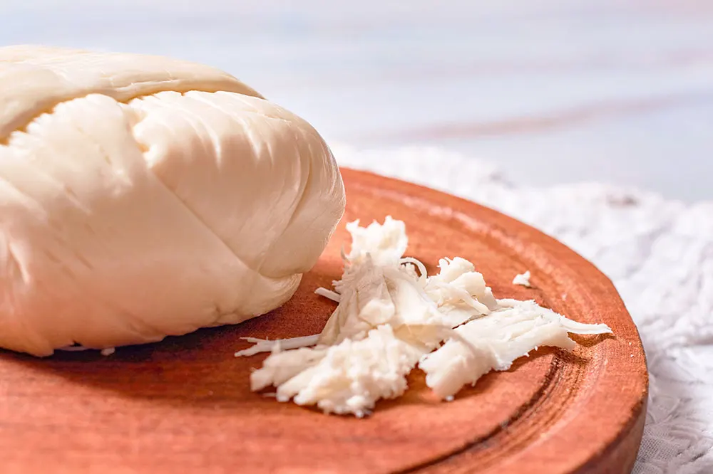 A ball of Quesillo with a few shredded pieces beside it in a brown plate served on a wooden table