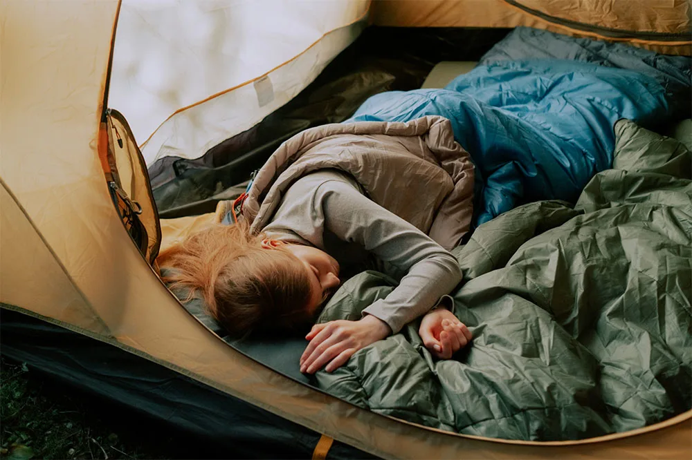 A person sleeping covered with a thermal blanket in a yellow tent while resting.
