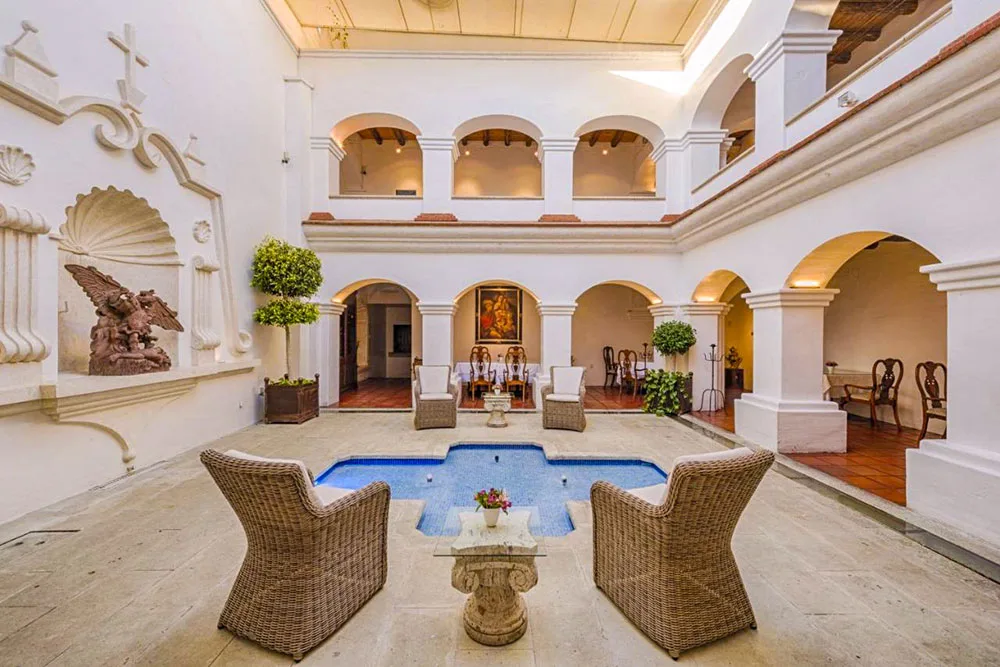 An open space of an indoor hotel with white walls with rattan chairs and a water fountain on the ground inside Palacio Borghese Hotel, one the best places on where to stay in Oaxaca