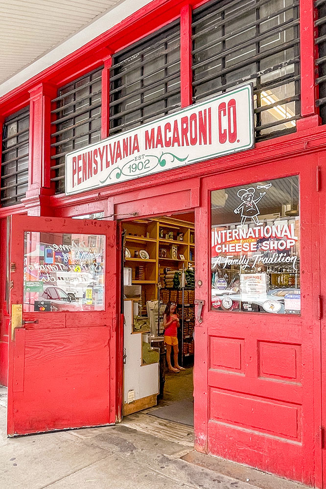 The open double red doors showing inside the Pennsylvania Macaroni Co.filled with cheese products with person inside.