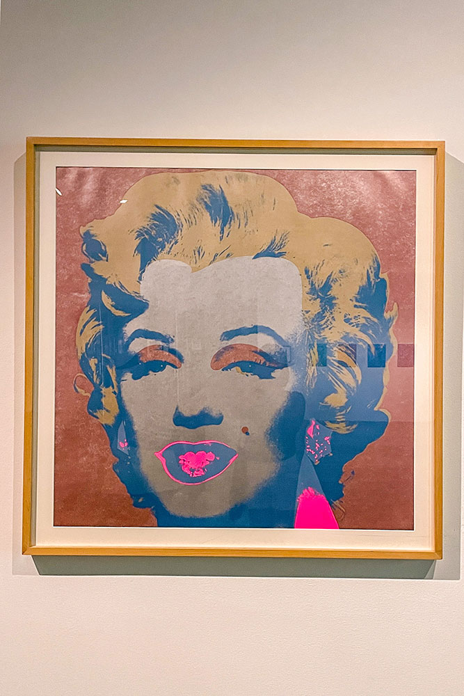 A colorful artwork of Marilyn Monroe in a frame protected by a glass cover on a white wall