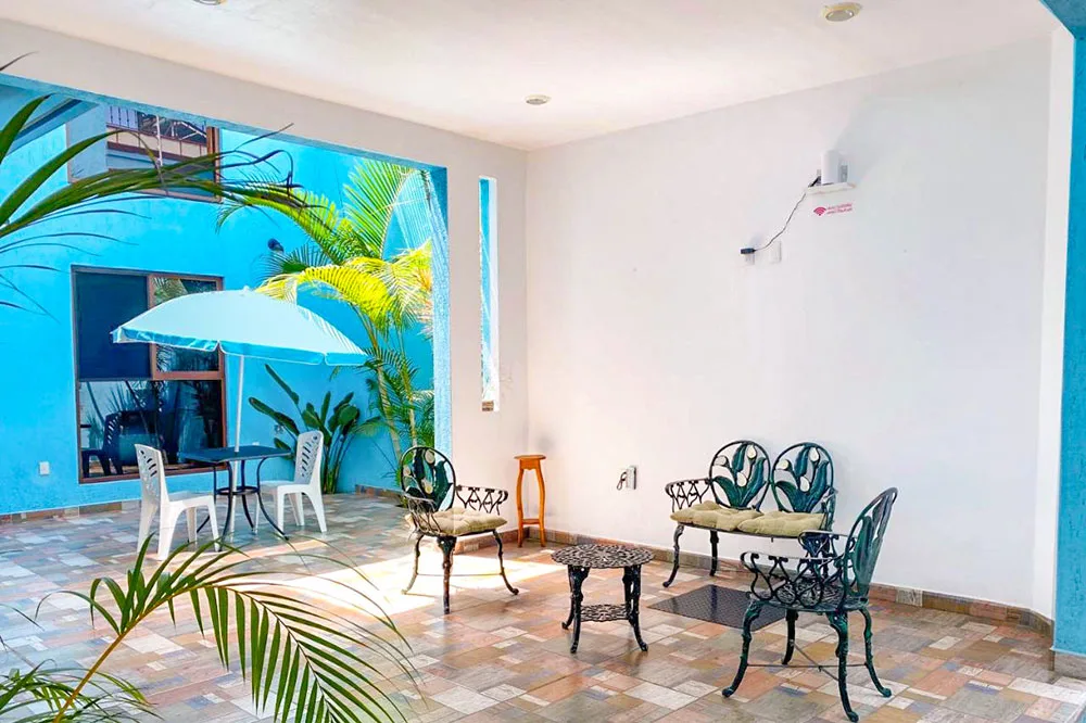 An open space with few metal chairs inside a white walled room with a view of a building with blue walls at a hostel in Oaxaca Mexico