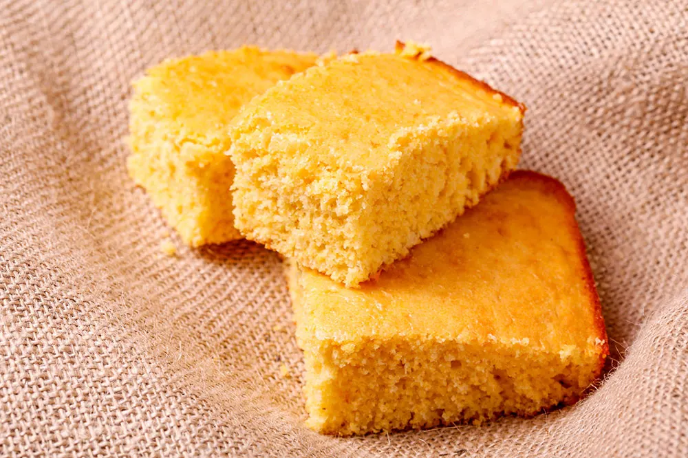 Square slices of Pan de elote, a corn cake served on a white cloth