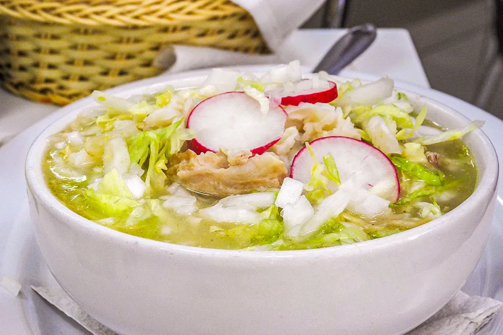 A soup with cabbage, onion, and meat slices served on a white bowl
