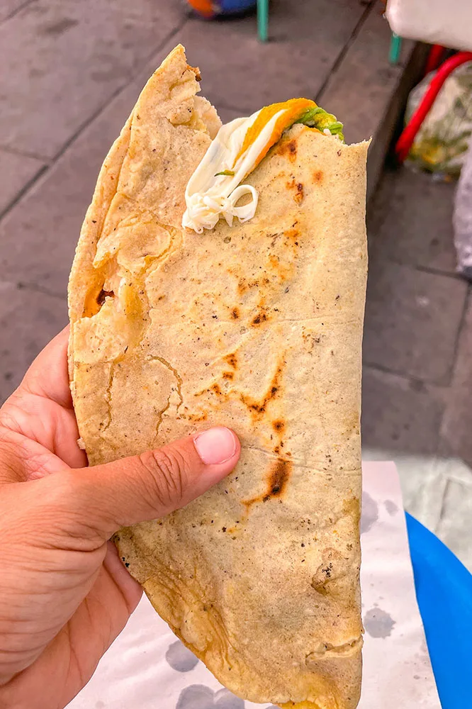 A hand holding Quesadillas bitten at the top with cheese oozing out