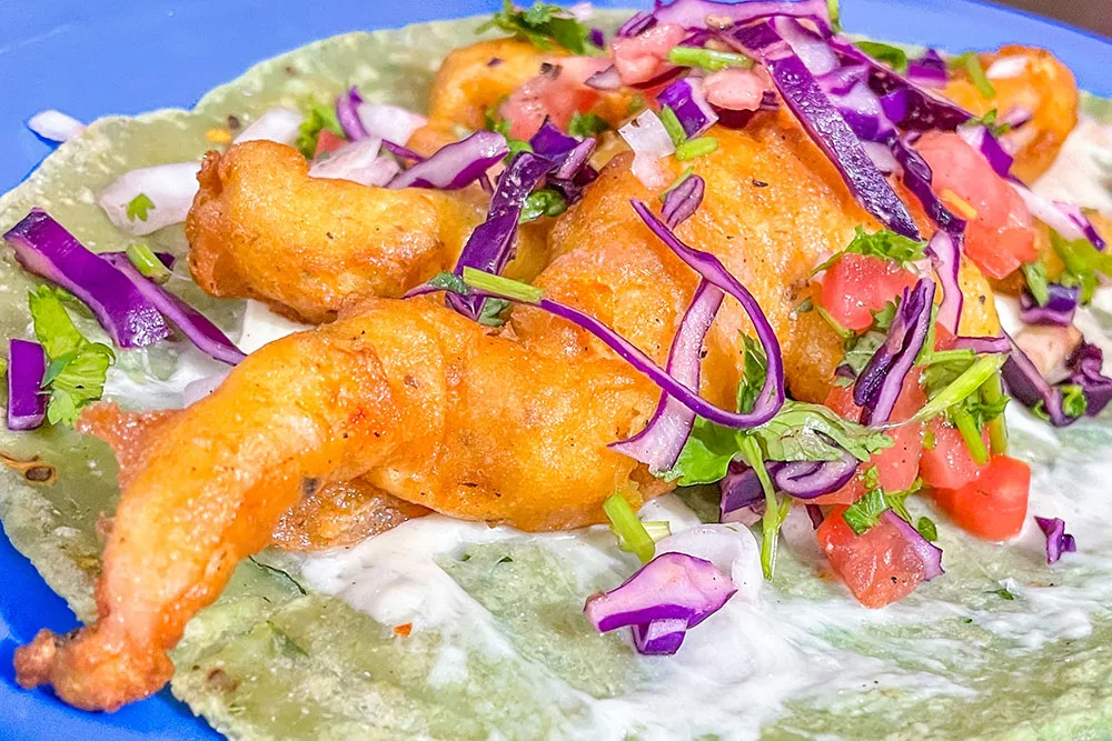 Tacos served open showign the fried prawns, cabbage slices, onion slices, and tomato slices filling