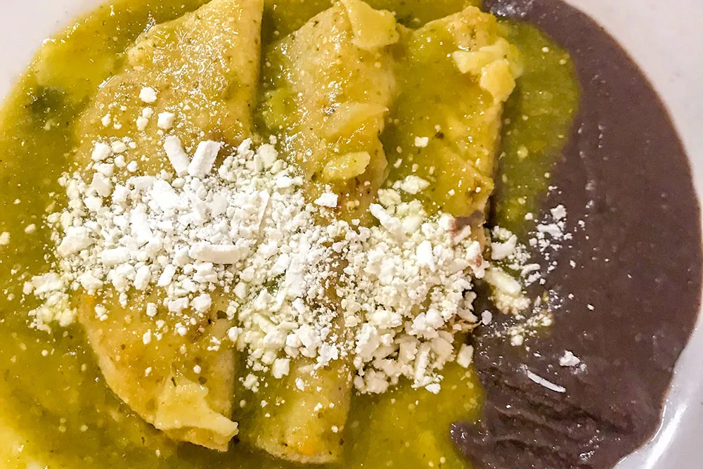 A plate of Enchilada, a Mexican food, topped with two enchilada sauces topped with cheese